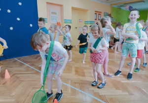 Dzieci za pomocą rakietki toczą piłkę slalomem do bramki